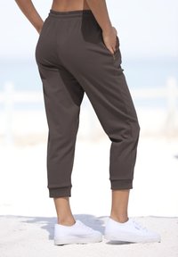Braune, kurze Jogginghosen aus weichem Stoff, mit seitlichen Reißverschlusstaschen und elastischen Bündchen, kombiniert mit weißen Turnschuhen.