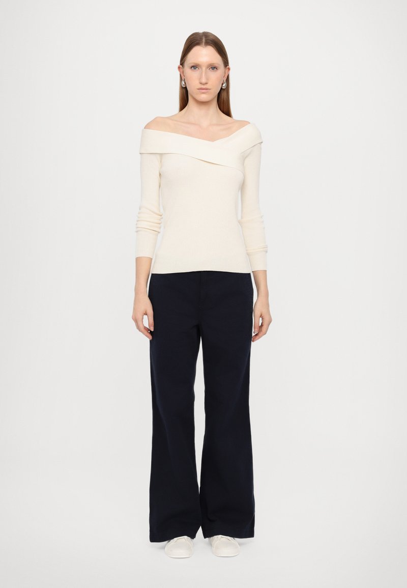 Off-white, gerippter Stricktop mit schulterfreier Gestaltung, kombiniert mit navyblauen, weit geschnittenen Hosen und weißen Slippern. Schlicht und modern.