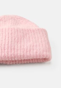 Gorro de malha rosa com uma textura suave, apresentando um padrão canelado e uma dobra na bainha. O material parece felpudo e quente.