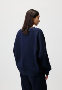 Sweatshirt bleu marine à col rond avec une coupe décontractée, des manches raglan, des poignets côtelés et un ourlet côtelé, fabriqué à partir d'un tissu doux et texturé.