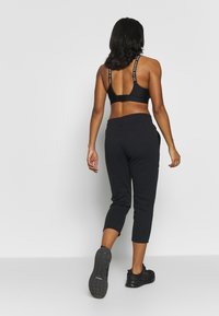 Schwarzer Sport-BH mit geradem Rücken und Logo-Trägern, kombiniert mit schwarzen, kurzen Sweatpants mit Taschen und einem Kordelzugbund. Schwarze Turnschuhe.