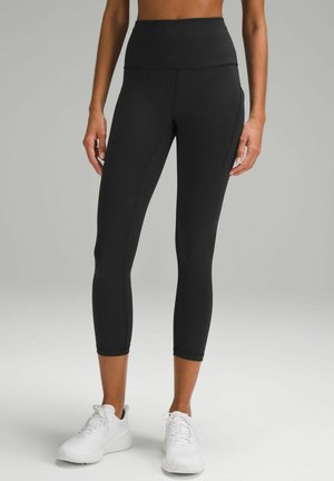 Zwarte sportlegging met hoge taille, cropped lengte en een gladde textuur, gecombineerd met witte sportschoenen.