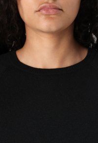 Svart genser med rund hals, ribbestruktur og mykt stoff. Nærbilde som fokuserer på halslinning og lepper, minimale synlige detaljer.