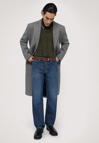 Šedý vlněný kabát, olivově zelený žebrovaný polo, modré rovné džíny, hnědý kožený opasek a černé kožené boty.