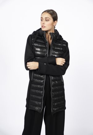 Zwarte gewatteerde vest met capuchon, voorzien van een quiltpatroon, een ritssluiting aan de voorkant en contrasterende gladde stof. Lange, strakke mouwen.