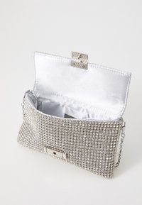 Silveraftendax med rhinestones, med ett satin-interiör och ett säkrat metallspänne. Inkluderar en kedjeslash.