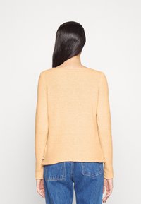 Hellpfirsichfarbener, langärmliger Pullover mit lockerer Passform, rundem Ausschnitt und weicher Textur, kombiniert mit blauen Jeans.