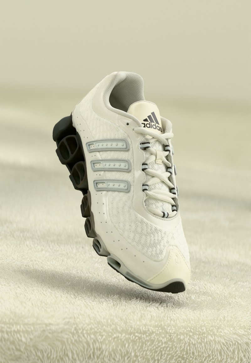 White Adidas running shoe with black segmented sole, mesh upper, and three signature stripes against soft beige textured background.