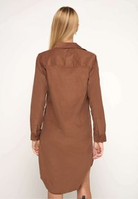 Robe chemise marron à boutons, à manches longues, coupe ajustée, col, fentes latérales et texture lisse, présentée de dos.