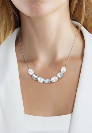 Perles irrégulières argentées et blanches sur un collier à fine chaîne en argent porté avec un blazer blanc et un haut.