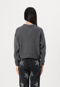 Grå strikket genser med en cropped design og ribbet kant. Bløtt stoff og løse ermer, kombinert med svarte bukser med stjerne mønster.