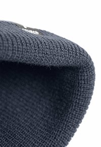 Tessuto lavorato a maglia blu navy con una superficie texture, caratterizzato da un bordo ripiegato e un piccolo etichetta nera con testo bianco.