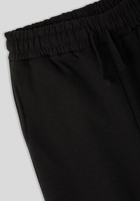 Pantaloni della tuta neri con fascia elastica in vita, coulisse e tessuto morbido, con dettagli evidenti sulla cucitura laterale.