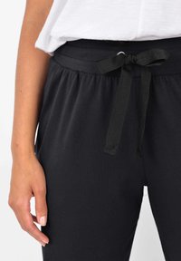 Svarta bomullsjoggers med elastisk midja och justerbar snörning. Slät textur, avslappnad passform och samlade sidor för komfort.