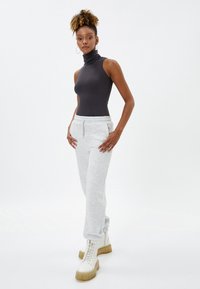 Top negro sin mangas con cuello alto combinado con pantalones de chándal gris claro y botas gruesas blancas con suela beige. Diseño de atuendo simple y casual.