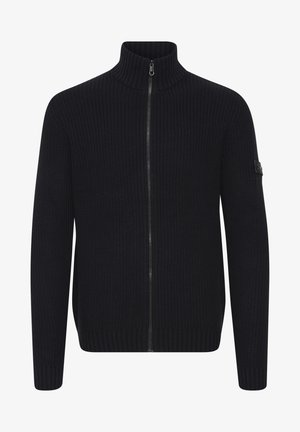 Pulover tricotat bleu marin cu guler înalt și închidere cu fermoar. Textură cu nervuri și manșete ajustate, având un mic accent cu logo negru pe mânecă.