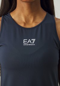 Sötét navy színű, ujjatlan felső, sima, rugalmas anyagból készült, középen, a mellkas területén fehér EA7 Emporio Armani logóval.