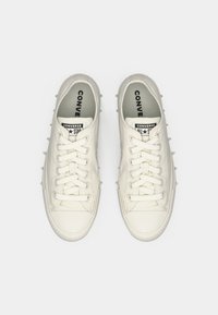 Baskets Converse blanches avec un design à lacets, semelle en caoutchouc texturée et accents en pointe sur les côtés. L'intérieur présente un rembourrage avec logo.