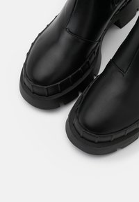 Bottes noires en cuir à la cheville avec un bout rond, une semelle en caoutchouc épaisse et des accents cloutés le long du bord. Fini mat et design sans couture.
