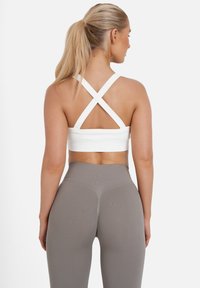 Top deportivo blanco recortado con tirantes cruzados en la espalda, combinado con leggings grises de tiro alto y ajustados. Textura suave, sin patrones visibles.