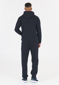 Sudadera azul marina con capucha ajustable, combinada con pantalones a juego. La tela parece suave; el diseño incluye puños acanalados y un ajuste relajado.