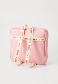 Rosa rektangulær veske laget av stoff, med beige stropper og teksten "TINY" i oransje. Jevn tekstur, glidelåsstenging på toppen.