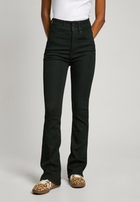 Black high-waisted jeans with a fitted top and flared legs, featuring two front buttons and a smooth texture. Paired with leopard print shoes.