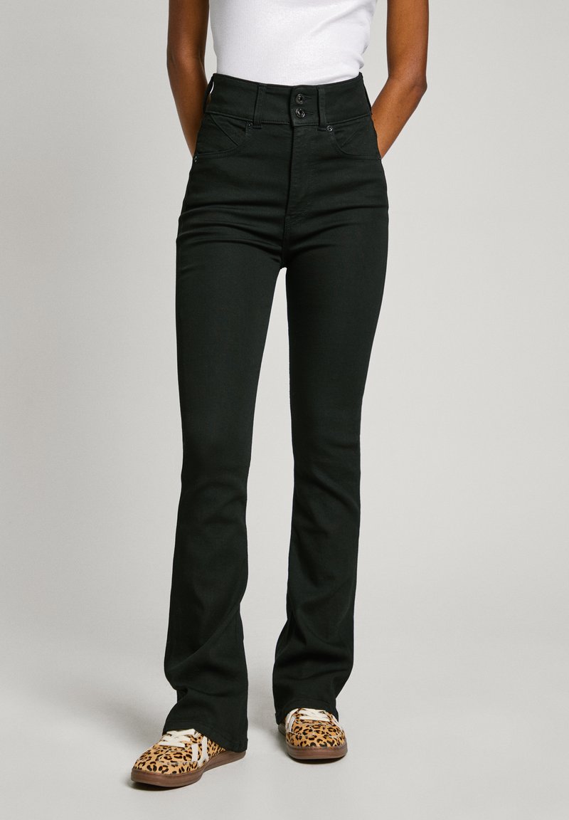 Black high-waisted jeans with a fitted top and flared legs, featuring two front buttons and a smooth texture. Paired with leopard print shoes.