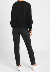 Zwarte oversized sweatshirt met een ronde halslijn en geribbelde manchetten, gecombineerd met slim-fit zwarte jeans en witte sneakers.