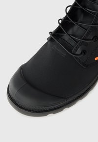 Black footwear featuring a smooth synthetic upper, textured laces, rubberized toe cap, and a woven sole detail. An orange accent is visible.