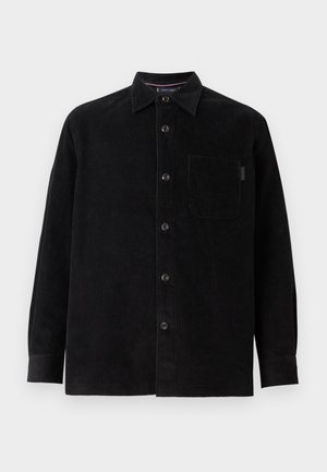 Camisa chaqueta de pana negra con cuello, cierre de botones en la parte delantera, mangas largas y un bolsillo en el pecho. Tejido texturizado con líneas verticales.