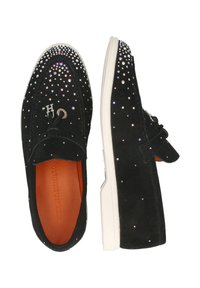 Zwarte suède instapschoenen met metallic uitziende studs, een witte rubberen zool en een decoratieve strik met een geborduurd logo op het bovenwerk.