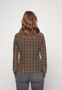 Camicia a quadri verdi con accenti rossi e neri, design aderente, maniche lunghe, polsini con bottoni e orlo arrotondato. Vista posteriore.
