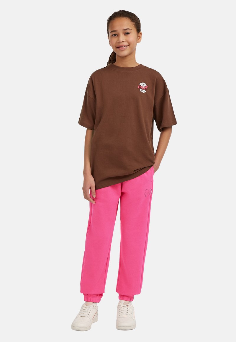 Brun bomullströja med korta ärmar och vit broderad detalj, i kombination med rosa sweatpants med mudd, bärs med vita sneakers.