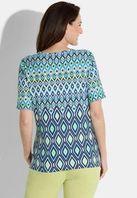 Korte mouwen top met een geometrisch diamantmotief in blauw, groen en marineblauw op een lichte stof met een ronde halslijn.