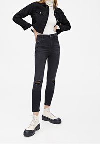 Chaqueta de mezclilla negra, suéter de cuello alto blanco, jeans ajustados desgastados de talle alto negros y botas de combate crema con suelas negras.