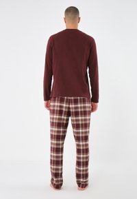 Långärmad burgundy topp i kombination med rutiga byxor i maroon, beige och vit; bomullstyg med mjuk textur.