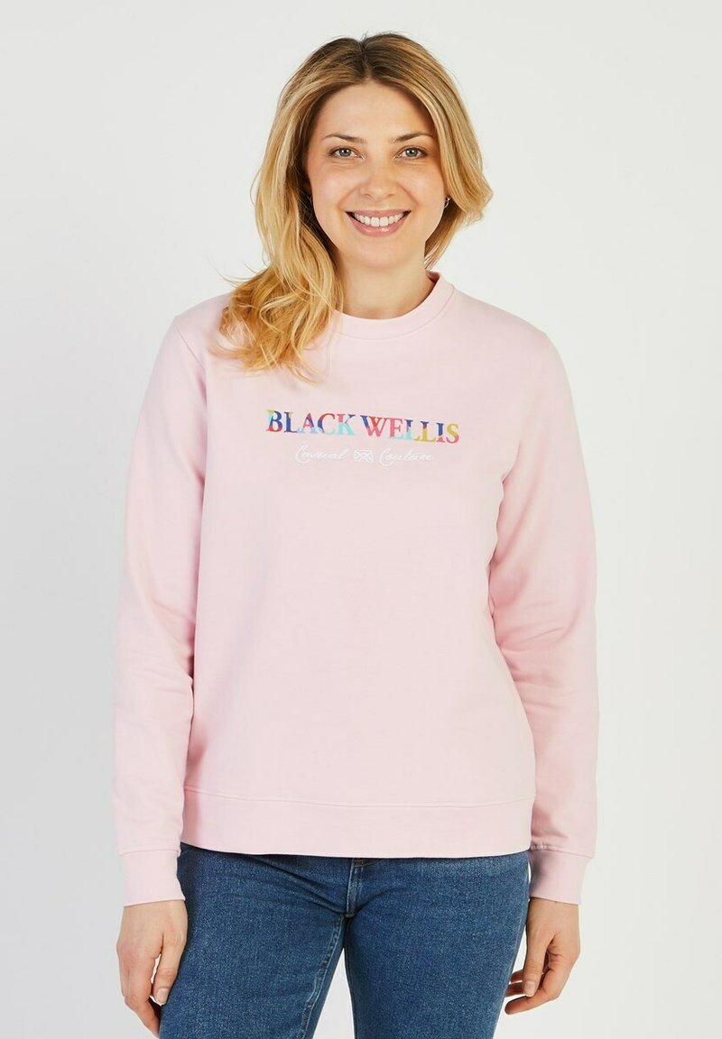 Sweatshirt en coton rose à manches longues, col rond, et logo brodé "BLACK WELLS" en texte coloré sur le devant.