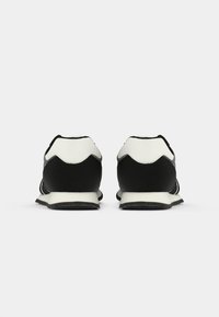 Black and white sneakers with a textured black upper, white accents, and a rounded toe design. The back features a scalloped edge.