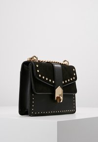 Czarna torebka wykonana z gładkiej skóry i zamszu, z złotymi akcentami, ćwiekami oraz łańcuszkowym paskiem.