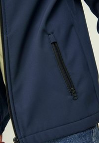 Chaqueta azul marino de tela lisa, con un bolsillo con cremallera en el lateral y costuras limpias a lo largo del dobladillo. Ideal para uso casual.