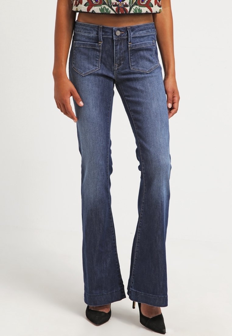 Jeans en denim foncé ajustés avec une coupe évasée, à cinq poches, avec une légère décoloration et des accents de couture subtils, assortis à des chaussures à talons hauts noires.