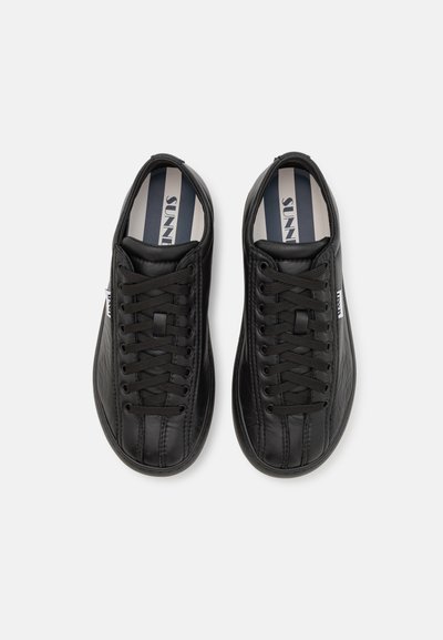 Adidași sintetici negri cu o finisare texturată, având șireturi, vârf rotund și o branț cu dungi și branding.