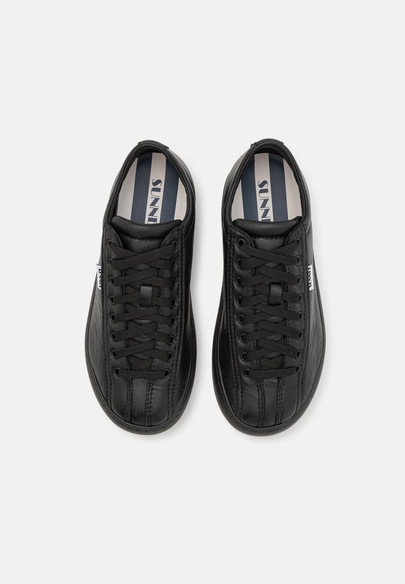 Black synthetic sneakers with a textured finish, featuring laces, a rounded toe, and a striped insole with branding.