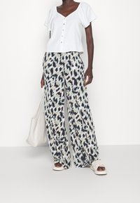 Biały top z krótkim rękawem, dekoltem w serek i guzikami, zestawiony z szerokimi spodniami o abstrakcyjnym niebiesko-zielonym wzorze.