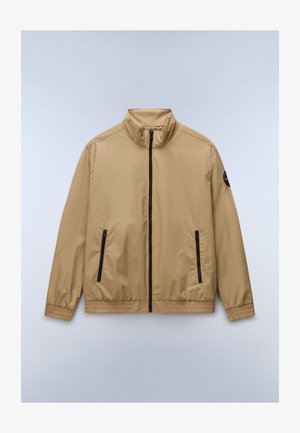 Beež kerge jope musta esemise luku, kahe vertikaalse lukuga tasku, elastsete mansettide ja vasakul varrukal oleva plaastriga.