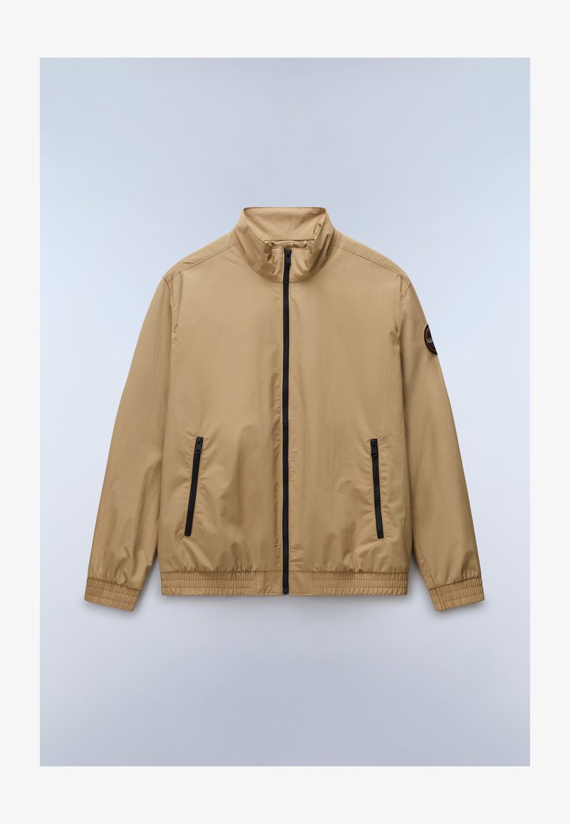 Μπεζ ελαφριά ζακέτα με μαύρο φερμουάρ στο μπροστινό μέρος, δύο κάθετες τσέπες με φερμουάρ, ελαστικές μανσέτες και ετικέτα στο αριστερό μανίκι.