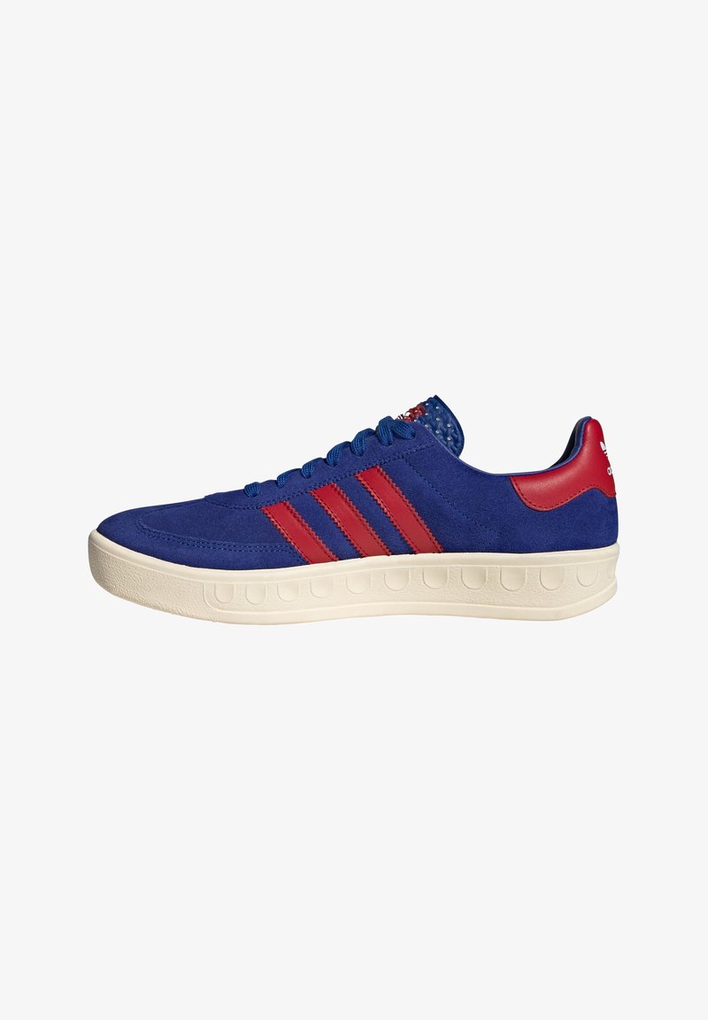 Blue suede sneaker with red stripes, a white rubber sole, and textured accents on the heel. Lace-up design with padded collar.