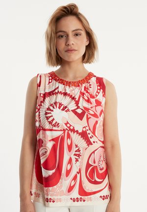 Top sans manches à motifs rouge et blanc avec un col froncé et des accents décoratifs orange. Tissu lisse avec un motif floral audacieux.