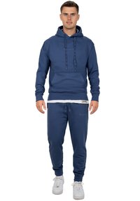 Marineblauwe katoenen hoodie met trekkoorden, een voorzak en bijpassende joggers met boorden. Gemaakt met witte sneakers.
